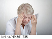 The elderly woman holds hands a head, going to accept tablets. Pain. Стоковое фото, агентство Ingram Publishing / Фотобанк Лори