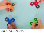 trendy fidget spinners - styled flat lay scene with hands holding colorful generic design spinners, copy space on blue background. fidget spinner, popular relaxing toy, generic design. Стоковое фото, агентство Ingram Publishing / Фотобанк Лори