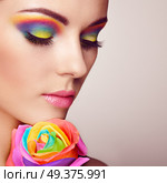 Portrait of beautiful young woman with rainbow rose. Bright colors. Long eyelashes, vivid colorful eyeshadows. Rainbow make up. Multicolored flowers. Стоковое фото, агентство Ingram Publishing / Фотобанк Лори