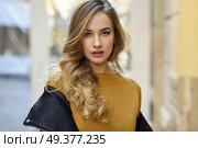 Blonde woman in urban background. Beautiful young girl wearing black leather jacket and mini skirt standing in the street. Pretty russian female with long wavy hair hairstyle and blue eyes. Стоковое фото, агентство Ingram Publishing / Фотобанк Лори