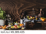 Various colorful tomatoes from garden, salad in plate, olives oil , mozzarella and kitchen tools on dark rustic table, front view. Still life. Стоковое фото, агентство Ingram Publishing / Фотобанк Лори