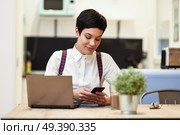 Young woman with very short haircut looking at her smart phone. Businesswoman working at home concept. Стоковое фото, агентство Ingram Publishing / Фотобанк Лори