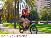 Girl riding e-bike in a city park with red t-shirt foldable ebike. Стоковое фото, агентство Ingram Publishing / Фотобанк Лори