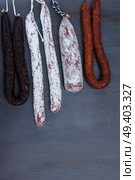 Cured meat and sausages hanging on black wooden background. Cured meat and sausages. Стоковое фото, агентство Ingram Publishing / Фотобанк Лори
