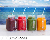 Colorful smoothy drinks in glass jars on white table by seaside. Fresh smoothy drink. Стоковое фото, агентство Ingram Publishing / Фотобанк Лори