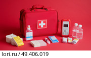 First aid kit displayed with essential medical supplies on a bright red background. Стоковое AI-изображение, AI-художник Сергей Толмачёв / Фотобанк Лори