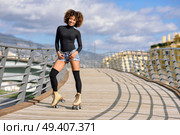 Black woman, afro hairstyle, on roller skates riding outdoors on urban bridge with open arms. Smiling young female rollerblading on sunny day. Beautiful clouds in the sky. Стоковое фото, агентство Ingram Publishing / Фотобанк Лори