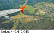 Airplane wing soaring over a picturesque landscape of green countryside, villages, and forests, offering a unique aerial perspective. Стоковое фото, фотограф Mikhail Davidovich / Фотобанк Лори