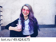 Happy beautiful teen with pink sunglasses drinks and enjoys a pink beverage sitting on urban ground. Стоковое фото, агентство Ingram Publishing / Фотобанк Лори