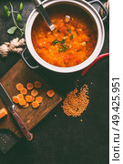 Cooking pot with tasty lentil soup and ladle on dark rustic kitchen table background with ingredients, top view with copy space. Healthy vegan food concept. Стоковое фото, агентство Ingram Publishing / Фотобанк Лори