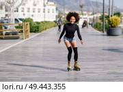 Young fit black woman on roller skates riding outdoors on urban street. Smiling girl with afro hairstyle rollerblading on sunny day. Black woman on roller skates riding outdoors on urban street. Стоковое фото, агентство Ingram Publishing / Фотобанк Лори