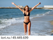 Young blonde woman with beautiful body in swimwear on a tropical beach with open arms. Caucasian female with straight long hairstyle wearing black bikini.. Young blonde woman with beautiful body in swimwear on a tropical beach with open arms. Стоковое фото, агентство Ingram Publishing / Фотобанк Лори