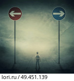 Surrealistic image as a man, with a bag in his back, stand in a foggy street in front of two huge road signs that show the left and right directions. Strategic journey, way of life and intuition concept. Стоковое фото, агентство Ingram Publishing / Фотобанк Лори