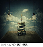 Idea concept with a boy standing on a pile of books trying to swich on the light bulbs, surrounded by concrete walls with clouds texture as thinking limitations. In search of knowlegde. Стоковое фото, агентство Ingram Publishing / Фотобанк Лори