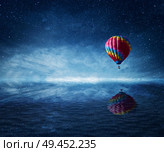 Hot air balloon flying over the a cold dark blue sea. Wonderful landscape with a starry night sky background and water reflection. Стоковое фото, агентство Ingram Publishing / Фотобанк Лори