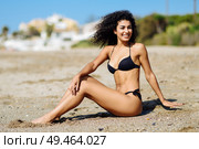 Young arabic woman with beautiful body in swimwear sitting on the beach sand. Smiling female with curly long hairstyle wearing black bikini.. Arabic woman with beautiful body in bikini lying on the beach sand. Стоковое фото, агентство Ingram Publishing / Фотобанк Лори