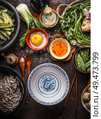 Empty asian bowl with chopsticks and ingredients for noodles meal with green vegetables and soba on dark rustic background with kitchen utensils, top view. Healthy asian cuisine. Asian food concept. Стоковое фото, агентство Ingram Publishing / Фотобанк Лори
