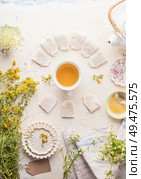 Cup with frame of tea bags of herbal tea on white table background, top view. Herbal tea setting with teapot , honey and fresh medical herbs and flowers. Copy space. Healthy preventive drink treatment. Стоковое фото, агентство Ingram Publishing / Фотобанк Лори