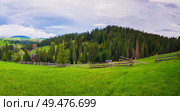 Picturesque spring Carpathians scene with wooden split rail fence across a green and lush pasture, and old cabins on the valley surrounded by pine woods. Стоковое фото, агентство Ingram Publishing / Фотобанк Лори