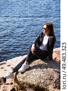 Woman Enjoying the Outdoors by the Water While Relaxing on a Rock During a Sunny Day. Стоковое фото, фотограф Aleksandr Golubev / Фотобанк Лори