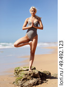 Caucasian woman practicing yoga at seashore. Young female standing on one leg while practicing the tree pose on a tranquil beach in Cadiz, Andalusia, Spain.. Caucasian blonde woman practicing yoga in the beach. Стоковое фото, агентство Ingram Publishing / Фотобанк Лори