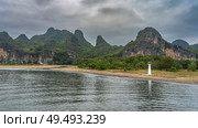 A white lighthouse is installed on the shore of a calm river. Ripples on the surface of the shiny water. Picturesque mountains against the sky and clouds. China. Li River. Li Jiang. Guilin. Стоковое фото, фотограф Вера Ивановна Кубарева / Фотобанк Лори