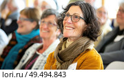 A diverse group of individuals sitting closely together in a row, engaging in conversation or observing an event. Стоковое AI-изображение, AI-художник Данила Большаков / Фотобанк Лори