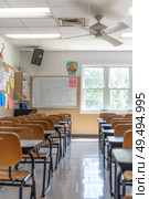 A room filled with numerous desks and chairs arranged neatly in rows, typical of a classroom setting. Стоковое AI-изображение, AI-художник Данила Большаков / Фотобанк Лори