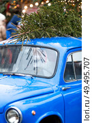 A Christmas tree is being carried on the roof of a vintage blue Christmas car. Decorated New Year's Moscow 2026. The concept of goods delivery. Стоковое фото, фотограф Photojuli / Фотобанк Лори
