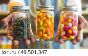 A person is standing, holding two jars overflowing with assorted candies, showcasing a variety of sweet treats. Стоковое AI-изображение, AI-художник Данила Большаков / Фотобанк Лори