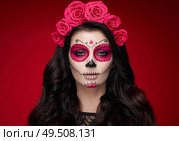 Portrait of a woman with sugar skull makeup over red background. Halloween costume and make-up. Portrait of Calavera Catrina. Стоковое фото, агентство Ingram Publishing / Фотобанк Лори