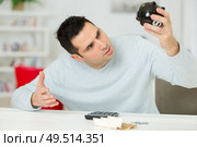 young man looking in desperation at his empty piggy bank. Стоковое фото, агентство Ingram Publishing / Фотобанк Лори