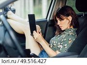 Young woman writing in a notebook with a pen in a white car pulling her feet out the window. Female wearing flowered shirt and shorts.. Woman writing in a notebook with a pen in a white car. Стоковое фото, агентство Ingram Publishing / Фотобанк Лори