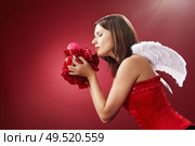 Girl with angelic wings smells petals of the roses, isolated on a red background. Стоковое фото, агентство Ingram Publishing / Фотобанк Лори
