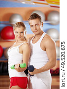 Two beautiful trainers with dumbbells in hands in sports club. Стоковое фото, агентство Ingram Publishing / Фотобанк Лори