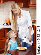 Mum pours milk in corn-flakes of the daughter on kitchen. Стоковое фото, агентство Ingram Publishing / Фотобанк Лори