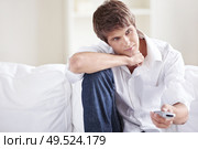 Attractive  man on the couch switches remote control TV channels. Стоковое фото, агентство Ingram Publishing / Фотобанк Лори