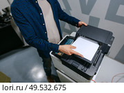 Person using a multifunction printer to copy documents in a modern office environment during daytime hours. Стоковое фото, фотограф Сергей Толмачёв / Фотобанк Лори