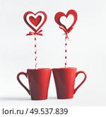 Two red mugs with hearts lollipop standing on white background. Declaration of love and Valentines day concept. Стоковое фото, агентство Ingram Publishing / Фотобанк Лори