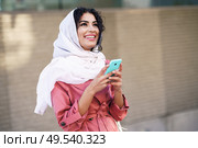 Young Muslim woman wearing hijab headscarf texting message with her smartphone in urban background.. Young Muslim woman wearing hijab texting message with her smartphone. Стоковое фото, агентство Ingram Publishing / Фотобанк Лори