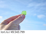 Hand holding green sanded glass up against a blue sky on an ocean shore. Стоковое фото, агентство Ingram Publishing / Фотобанк Лори