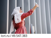 Young Arab Woman wearing hijab headscarf photograph with a smartphone outdoors.. Arab Woman with hijab taking selfie with smartphone. Стоковое фото, агентство Ingram Publishing / Фотобанк Лори