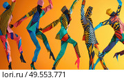 A group of dancers in vibrant, geometric-patterned costumes leaping in unison. Стоковое AI-изображение, AI-художник Данила Большаков / Фотобанк Лори