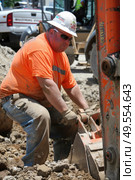 A man wearing an orange shirt and white hat is actively engaged in work at a construction site. Стоковое AI-изображение, AI-художник Данила Большаков / Фотобанк Лори