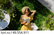 Woman relaxing in garden reading a book on a sunny day surrounded by flowers and greenery. Стоковое AI-изображение, AI-художник Сергей Толмачёв / Фотобанк Лори