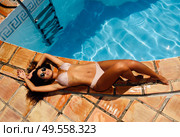 Top view of beautiful young woman with sunglasses lies on the edge of the swimming pool, sunbathing, tanned perfect body, curly long hair, fashionable bright bikini. Beautiful woman with sunglasses lies on the edge of the swimming pool. Стоковое фото, агентство Ingram Publishing / Фотобанк Лори
