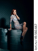 redheaded model girl in a long dress in a dark industrial Studio near barrels of oil. Стоковое фото, агентство Ingram Publishing / Фотобанк Лори