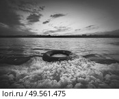 Old vehicle tire thrown on the shore of a pond, covered with fluffy surf foam generated by waves. Scenery sunset view, moody and dramatic background. Environment pollution and ecology concept. Стоковое фото, агентство Ingram Publishing / Фотобанк Лори