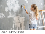 A little girl paints a wall in a new house. Interior decoration of the house, wall painting. Cosmetic repairs. Child labor. Стоковое AI-изображение, AI-художник Photojuli / Фотобанк Лори