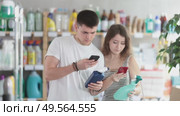 Man and a woman scan the barcode of the cleaning spray and read the detailed instructions. Customers use a modern payment method using the bank's mobile application. Стоковое видео, видеограф Яков Филимонов / Фотобанк Лори